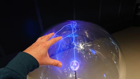 A hand touching a glass globe filled with charged plasma, making lightning effects where the fingertips touch the glass.